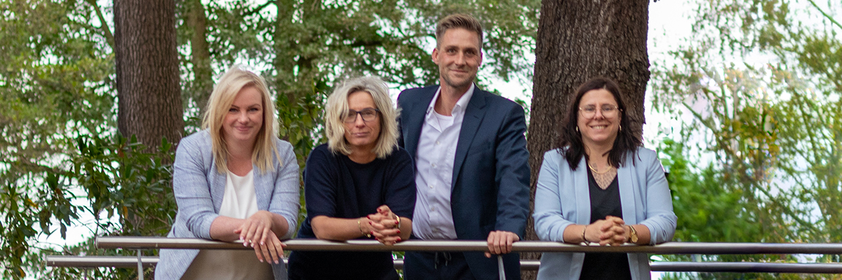 Die Mitarbeiter von Spree immobilien als Porträtfoto an einer grünen Wand. Davor stehen ein Sofa und eine Palme.