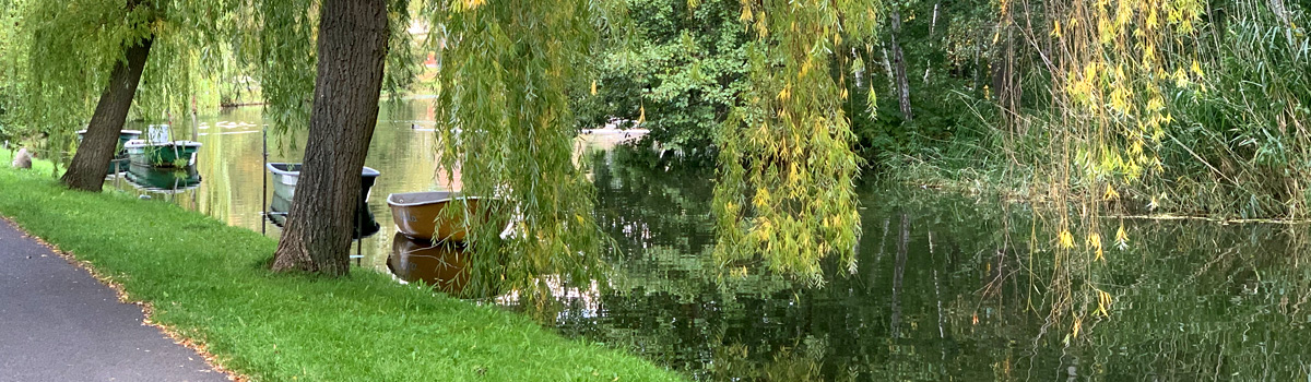 Spreepromenade mit Weiden und Booten am Ufer.
